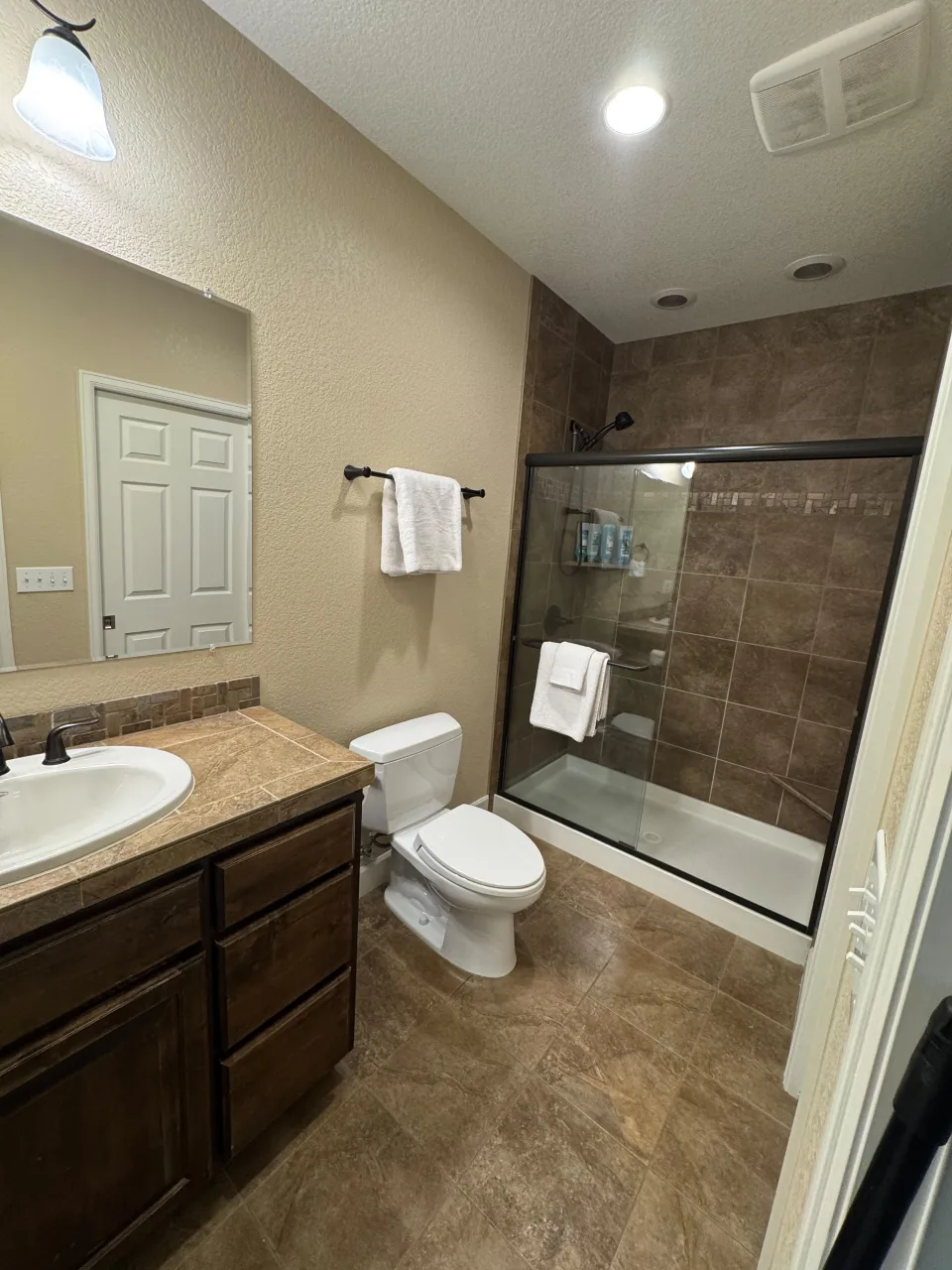 Baño impecable con ducha de vidrio, azulejos marrones, inodoro y lavamanos relucientes tras una limpieza profesional