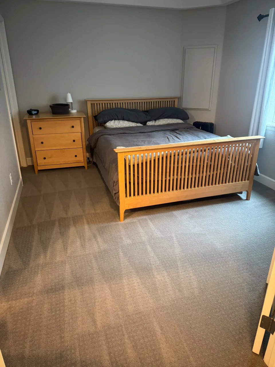 Dormitorio principal limpio y ordenado con cama de madera, cómoda y alfombra recién aspirada con líneas de limpieza visibles